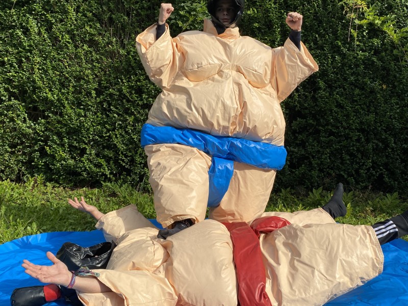 Deux personnes en tenues de sumo gonflables s’affrontent dans une ambiance ludique et amusante. Les costumes volumineux ajoutent du fun à leur duel, offrant un spectacle divertissant.