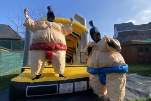 Deux personnes en tenues de sumo gonflables s’affrontent dans une ambiance ludique et amusante. Les costumes volumineux ajoutent du fun à leur duel, offrant un spectacle divertissant.