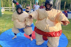 Deux personnes en tenues de sumo gonflables s’affrontent dans une ambiance ludique et amusante. Les costumes volumineux ajoutent du fun à leur duel, offrant un spectacle divertissant.